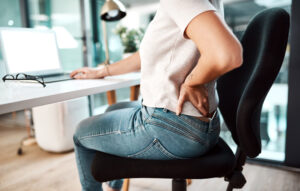 Woman sitting at an office desk holding her back from pain
