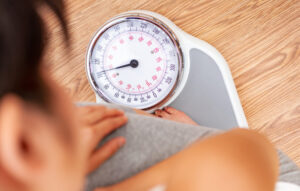 Woman on scale wondering if eating fat or carbs makes her gain weight