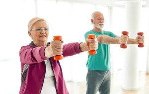An elderly couple exercising with dumbbells to strengthen their shoulders